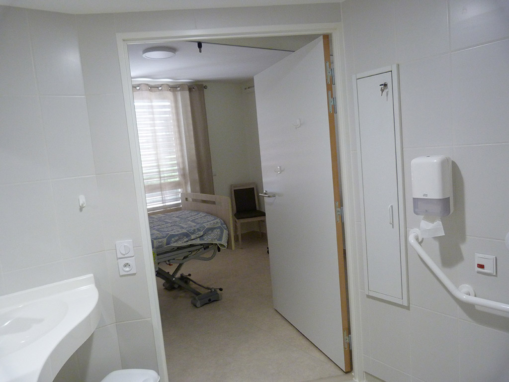 Reconstruction d'un EHPAD dans le Médoc - La chambre et son cabinet de toilette - Optimisation de l'espace par le mobilier Chambre vue depuis la salle de bain BOSSEGE